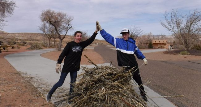 Two Grand Canyon Youth alumni high fiver over a pile of brush Service project pandemic pickup